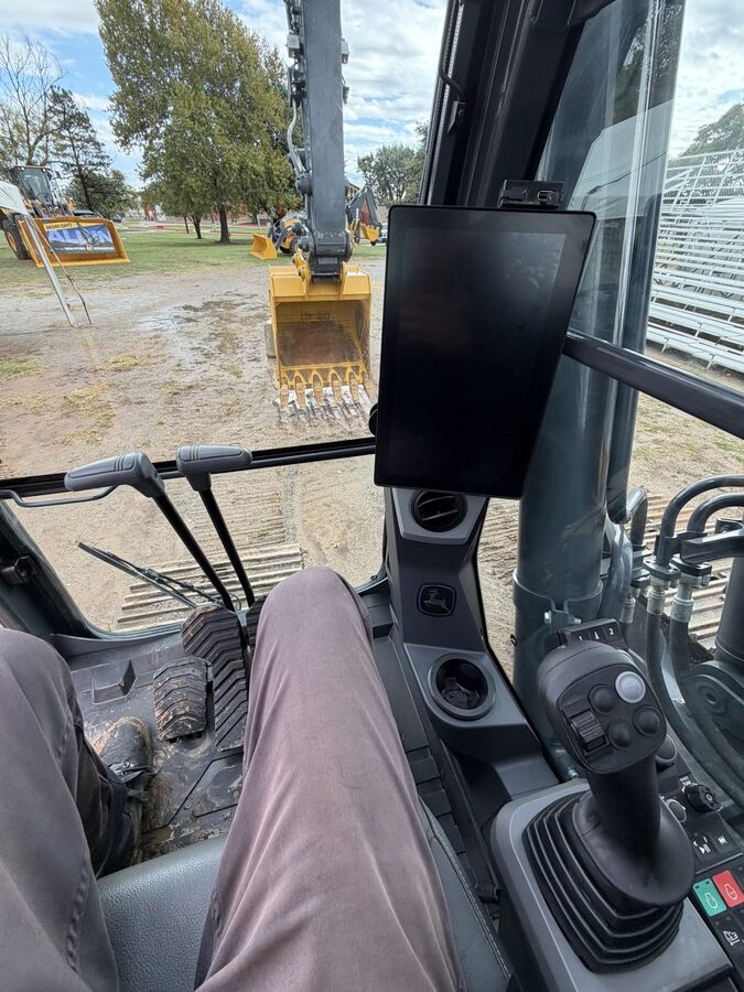 The view from the operator seat of a John Deere P-Tier excavator: the G5 Plus display, the joysticks and the bucket out front