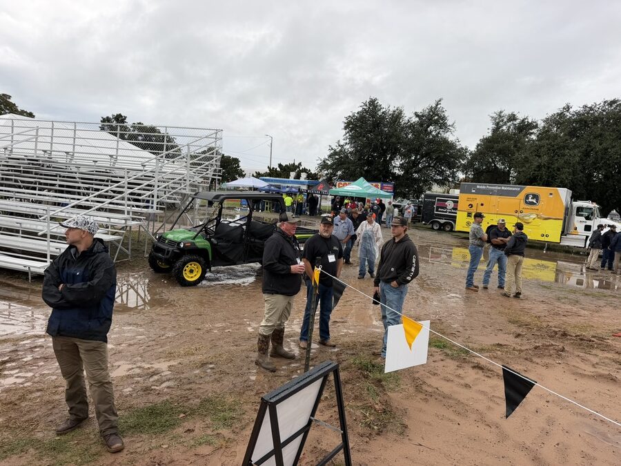 Customers in rain gear at the bleachers on Demo Day, with flags marking the demo pads and mud underfoot