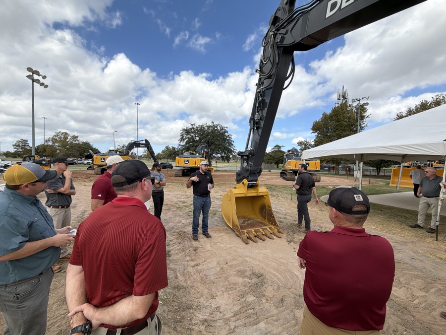 The CL Boyd team on the bleachers at the Tuesday walkthrough with the excavators set on the demo pads under a blue sky